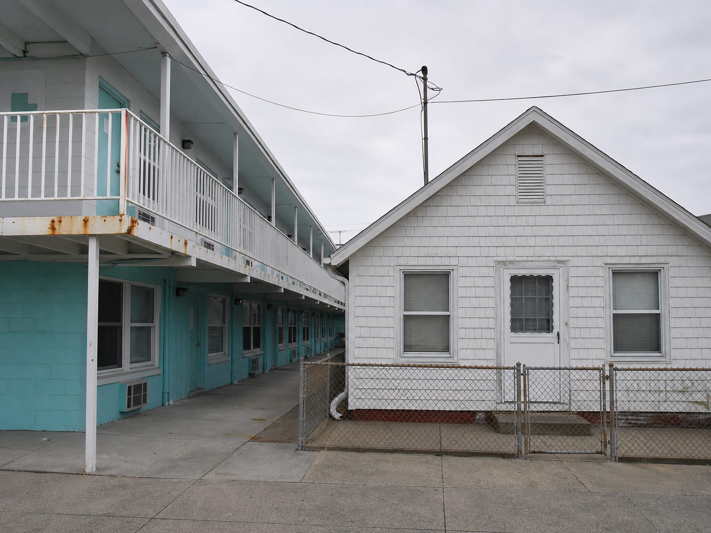 A motel form guest accommodation building with exterior access walkways standing directly against a small attached gabled house in Wildwood, New Jersey, two entirely different envelopes meeting at one lot line