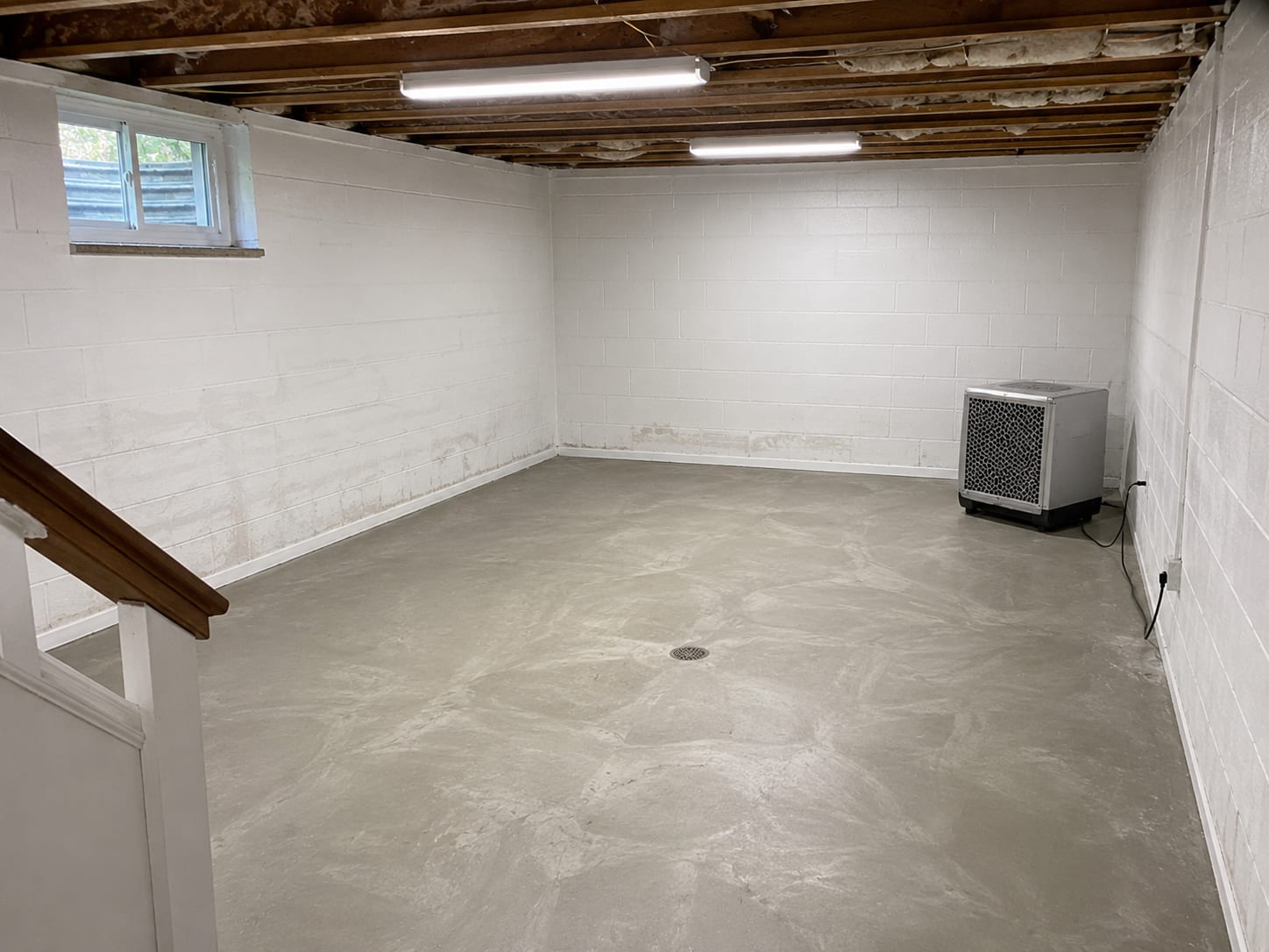 Freshly remediated basement room with clean white-painted concrete block walls, sealed floor, and HEPA air scrubber unit running in the corner