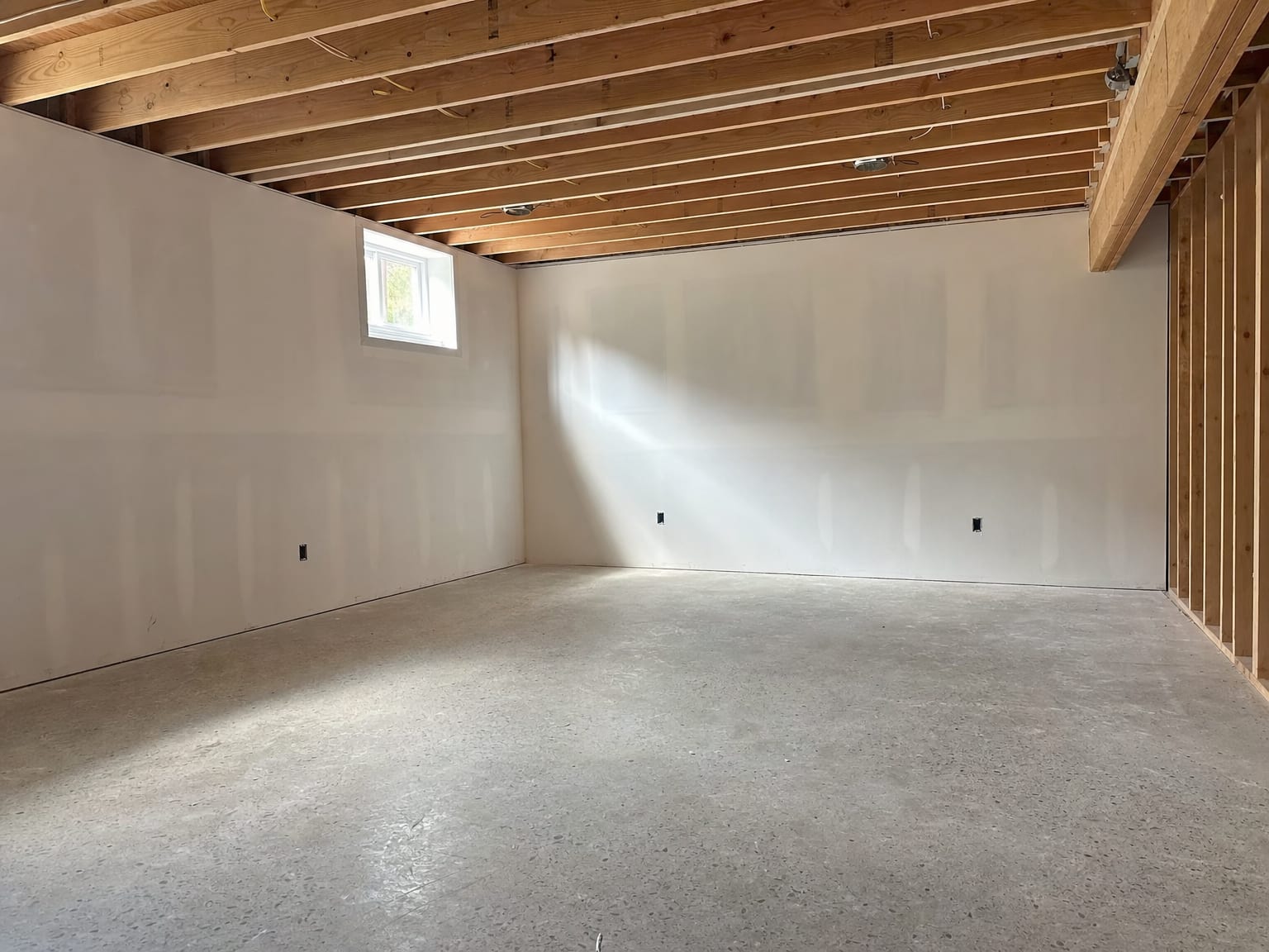 Fully reconstructed basement utility room with new insulation batts visible between studs and a clean painted concrete floor ready for final inspection