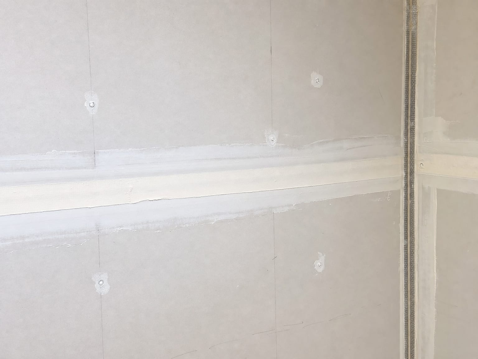 Close view of freshly taped and mudded drywall seams on a newly installed wall during residential reconstruction after water damage