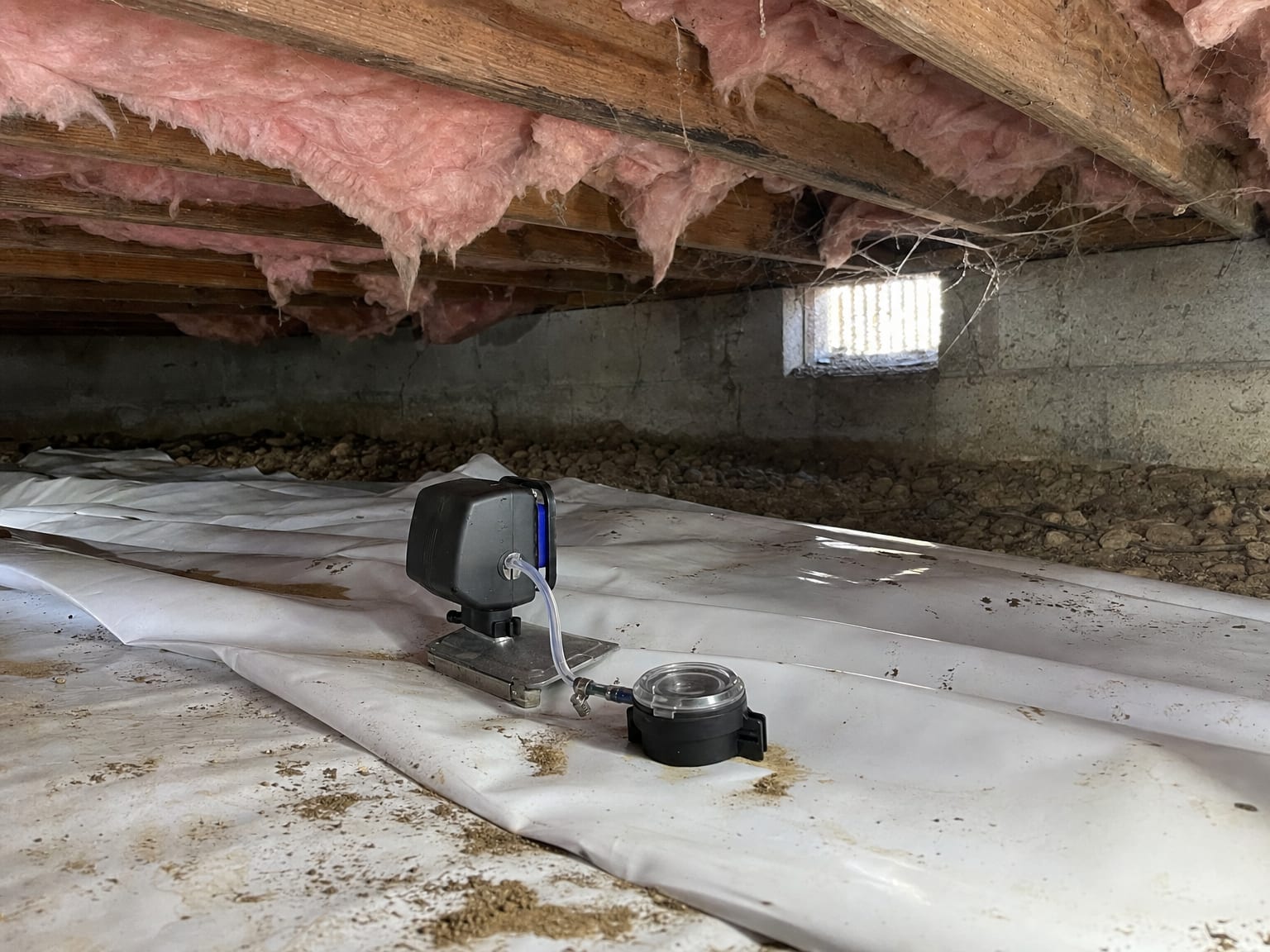 Unfinished attic interior of a New Jersey cape cod home showing wooden rafters, fiberglass insulation batts, and a thermal imaging camera resting on a joist