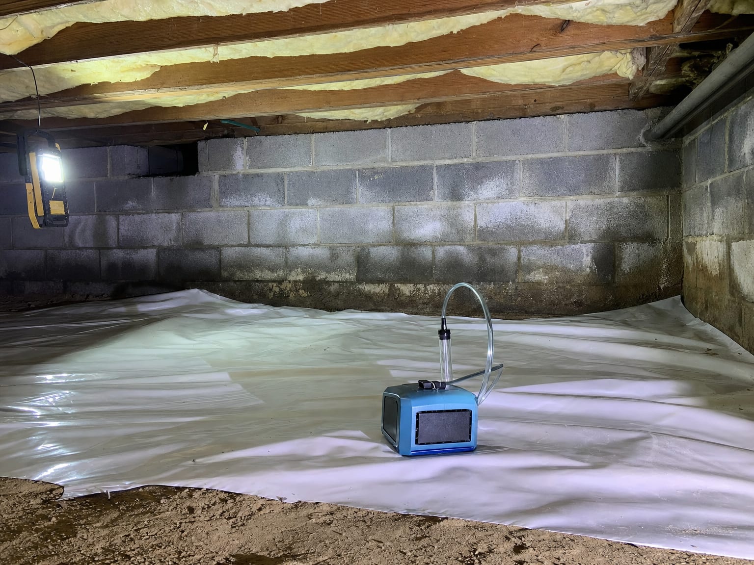 Air sampling pump on a vapor barrier in a residential crawl space with visible concrete block walls and insulation overhead