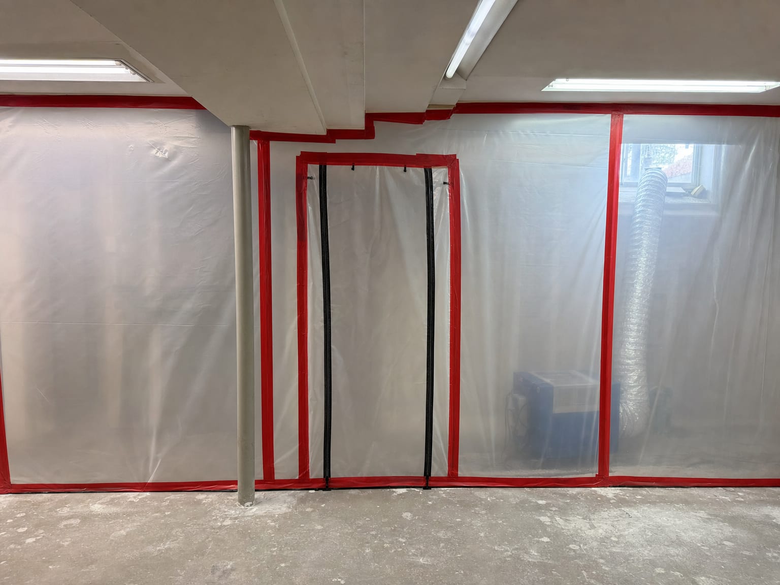 Freestanding HEPA air scrubber unit with flexible exhaust ducting running through a small window opening in a remediated New Jersey basement